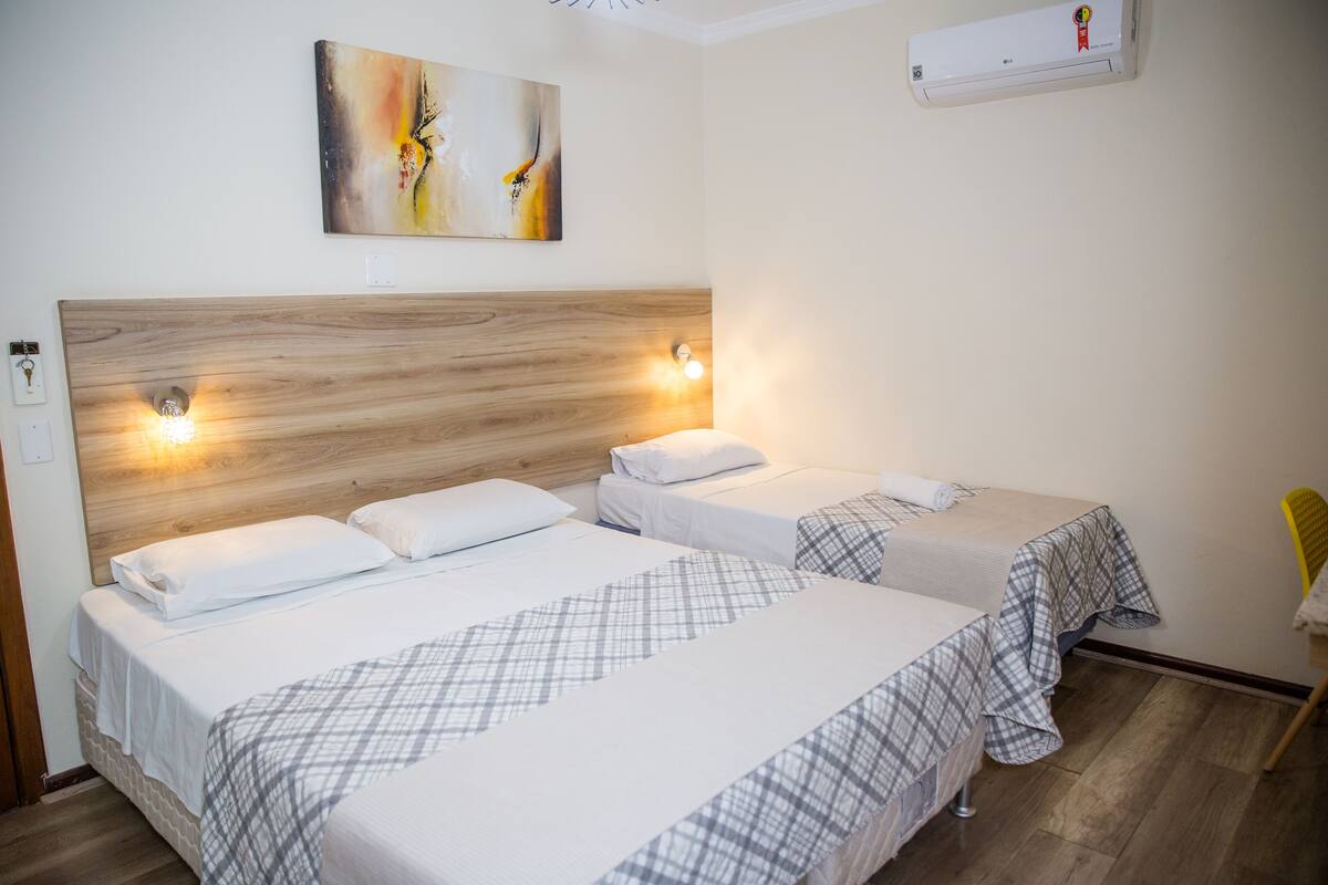 Une chambre d’hôtel avec deux lits, une tête de lit en bois, un climatiseur fixé au mur et un tableau.