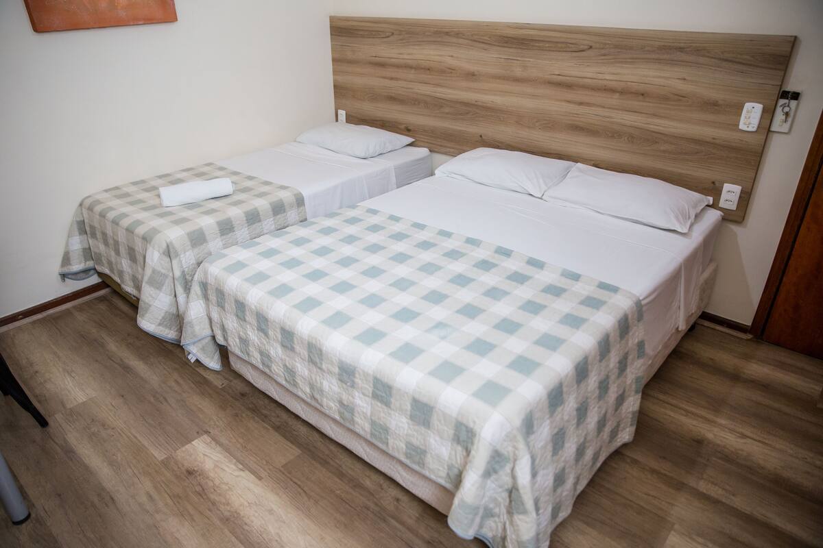 Une chambre d’hôtel avec deux lits simples, une tête de lit en bois et une couvre-lit à carreaux.