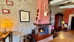 Ein rustikales Interieur mit einer Steinwand, einem Kamin mit Hirschgeweih und gerahmten Bildern an der Wand.