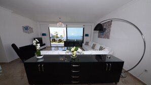 A modern living room with a black sofa, a glass coffee table, and a TV. There is a view of the ocean through large windows. - Contemporary Villa, amazing sea views, heated infinity pool, daily maid service (Kiziltas, Kalkan)