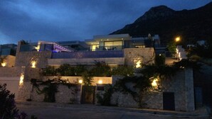 A modern building with a glass facade, stone walls, and outdoor lighting. - Contemporary Villa, amazing sea views, heated infinity pool, daily maid service (Kiziltas, Kalkan)