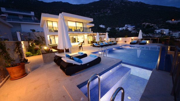 A modern outdoor pool area with lounge chairs and umbrellas, surrounded by a mountain backdrop. - Contemporary Villa, amazing sea views, heated infinity pool, daily maid service (Kiziltas, Kalkan)