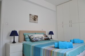 A bedroom with a bed, two bedside tables, a nightstand, a wall-mounted lamp, a painting, and a wardrobe. - 'KATIKIES 22' Luxury Detached Pissouri Beach Properties, Great Relaxing Location (Pissouri)