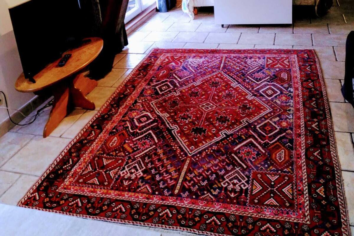 A bedroom with a sloped ceiling, a bed with a colorful bedspread, a red patterned rug, and a small wooden table with a chair.