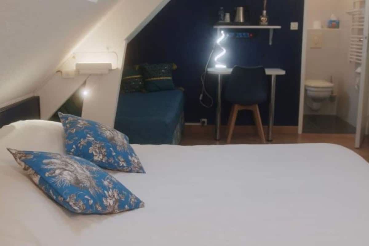 A bedroom with a bed, two pillows, a desk, and a chair.