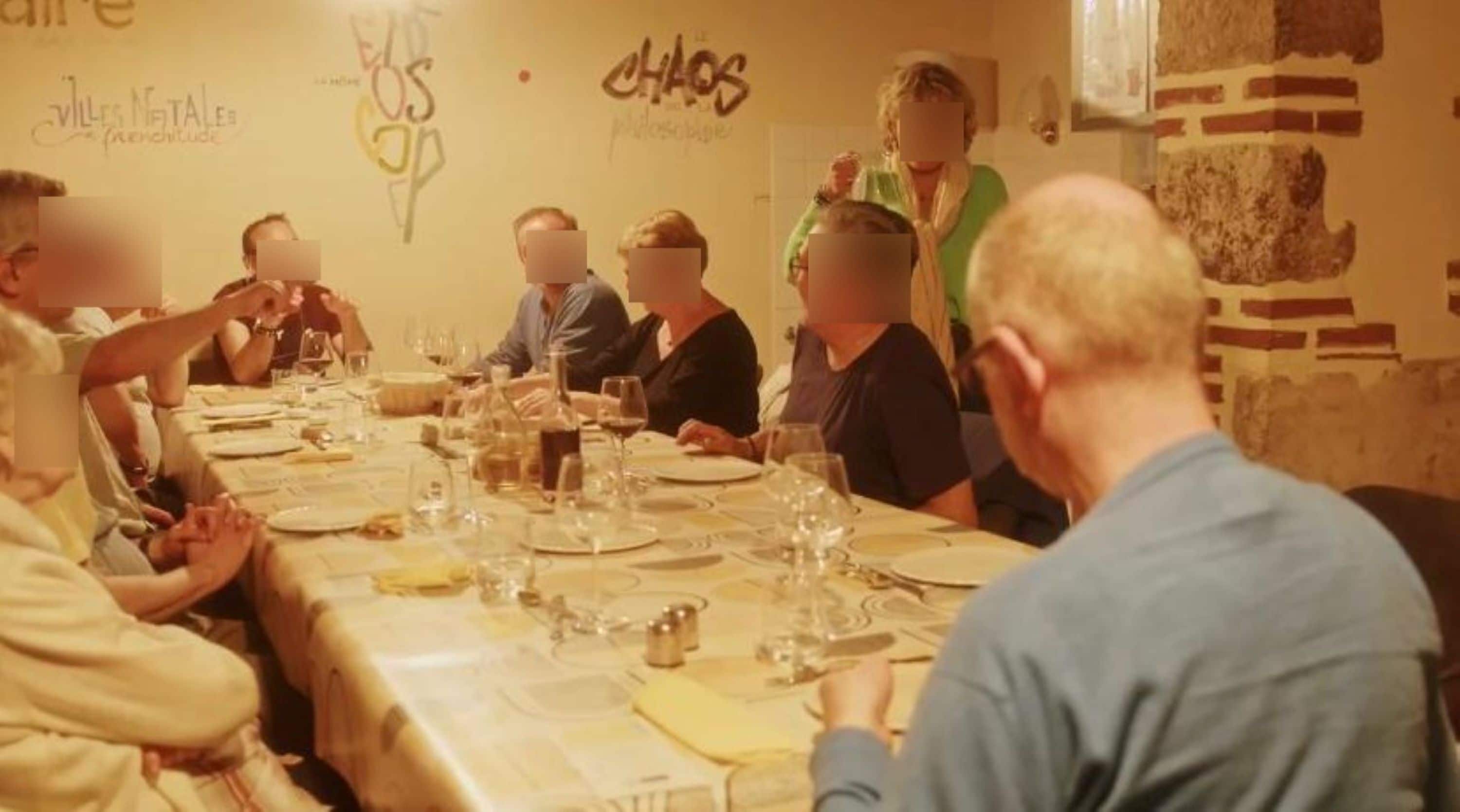 Un groupe de personnes est assis autour d’une table dans une pièce aux murs en briques, ornée d’une fresque.