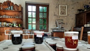 A kitchen with jars of preserves on a counter, a wooden shelf with kitchenware, and a window with greenery outside. - Maison Cerviña (Germigny-des-Pres)