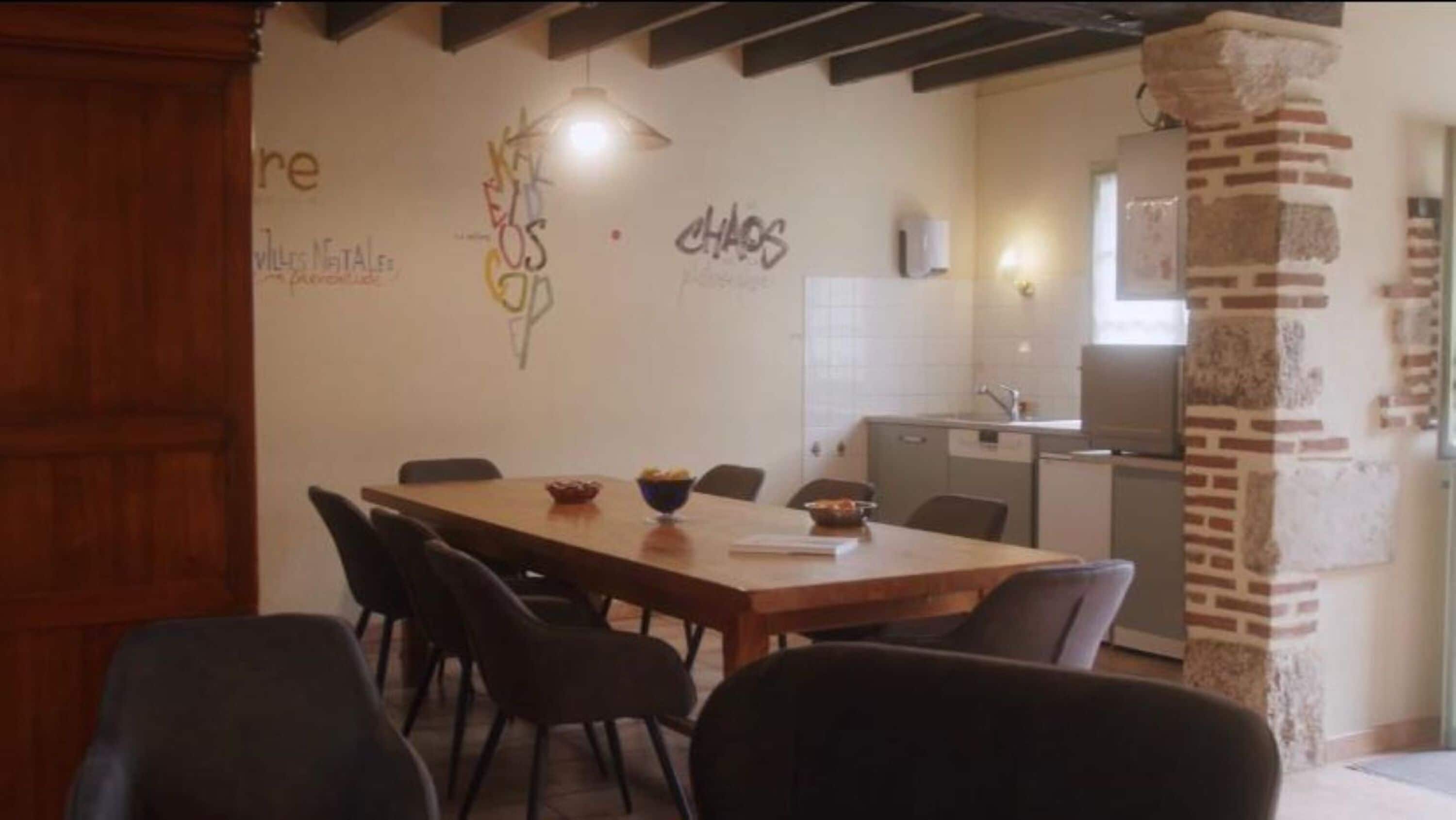 Un coin repas avec une table et des chaises en bois, une cuisine en arrière-plan et une colonne en briques.