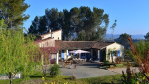 A two-story building with a tiled roof, a patio area with outdoor furniture, and a view of the surrounding trees and landscape. - Villa with Pool, Privacy and Magnificent View (Barbentane)