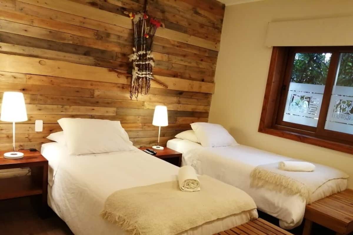 A room with two beds, wooden walls, a window with a view, and a decorative hanging.