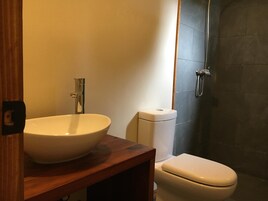 Un baño con tocador de madera, lavabo blanco, inodoro y zona de ducha.