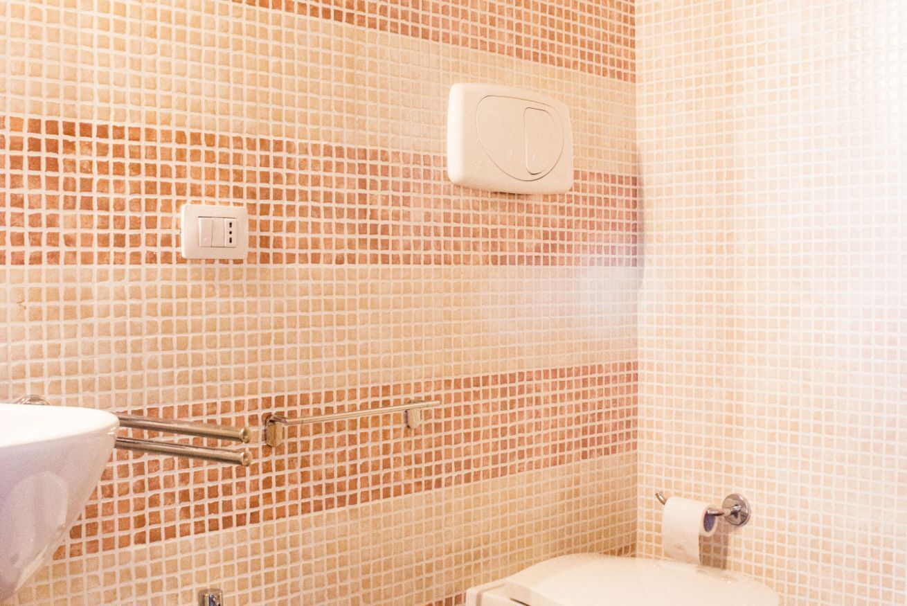 Ein Badezimmer mit gefliestem Boden, einem weißen Waschbecken, einer Toilette und einem Wandtrockner.