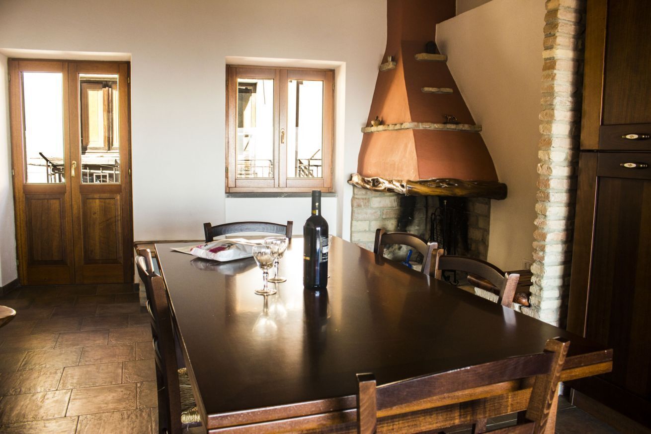 Uma sala de jantar com mesa de madeira, cadeiras, janela e lareira de tijolos.