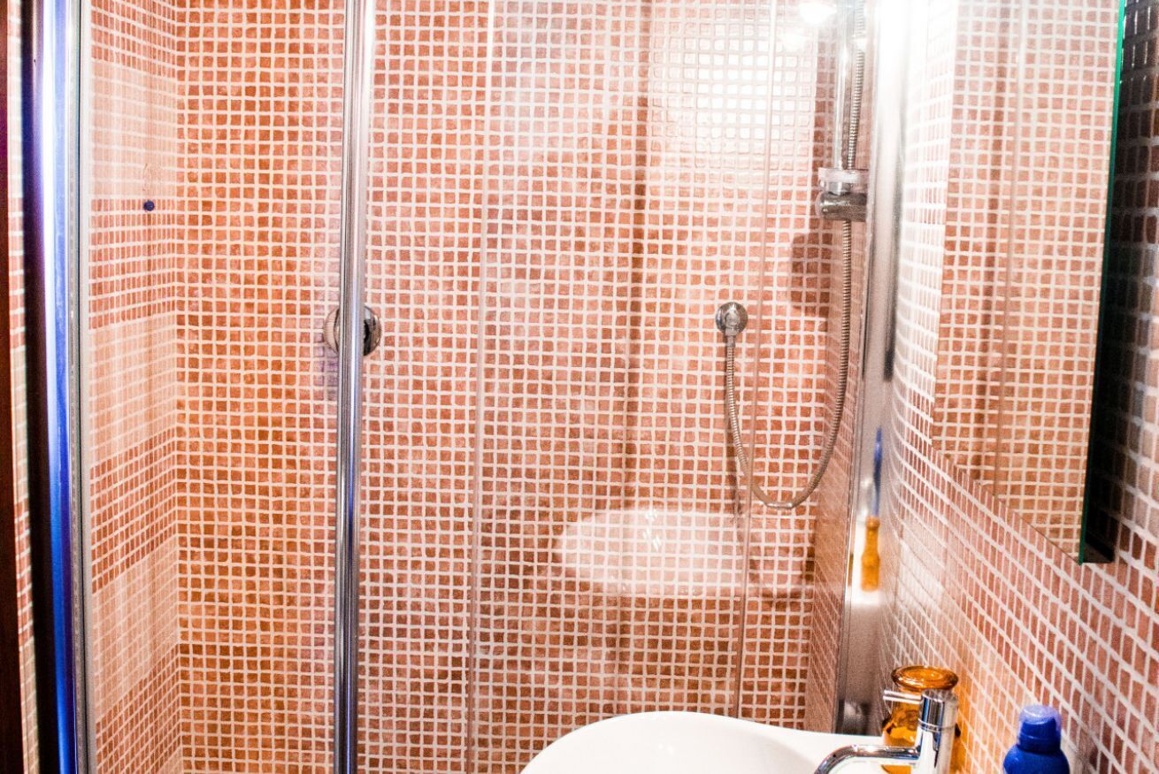 Ein Badezimmer mit Duschbereich, der durch eine Glastür abgegrenzt ist, geflieste Wände und einem Waschbecken mit Spiegel.