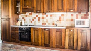A kitchen with wooden cabinets, a tiled backsplash, a stove, and a microwave. - Su Terrassu by All4sardinia  (Ulassai)