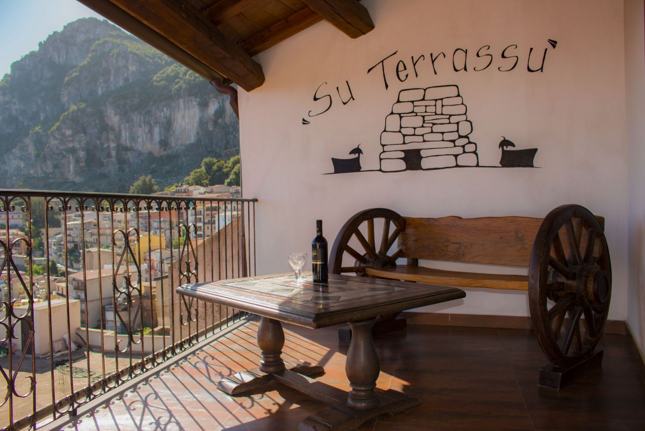 A balcony with a table, a bench, and a wall with the text "Su Terrassu".