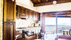 A kitchen with wooden cabinets, a dining table set with wine glasses, and a view of the outdoors. - Su Terrassu by All4sardinia  (Ulassai)