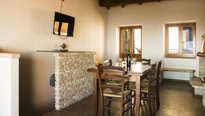 A dining area with a stone wall, wooden chairs, a table, and a TV mounted on the wall. - Su Terrassu by All4sardinia  (Ulassai)