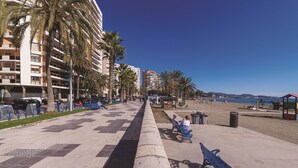 A coastal promenade with palm trees, a beach, and a row of buildings.