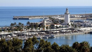 A coastal cityscape with a prominent lighthouse, marina, and a sea wall.