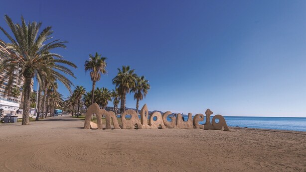 A beach with palm trees and a large sand sculpture spelling "Malaga".