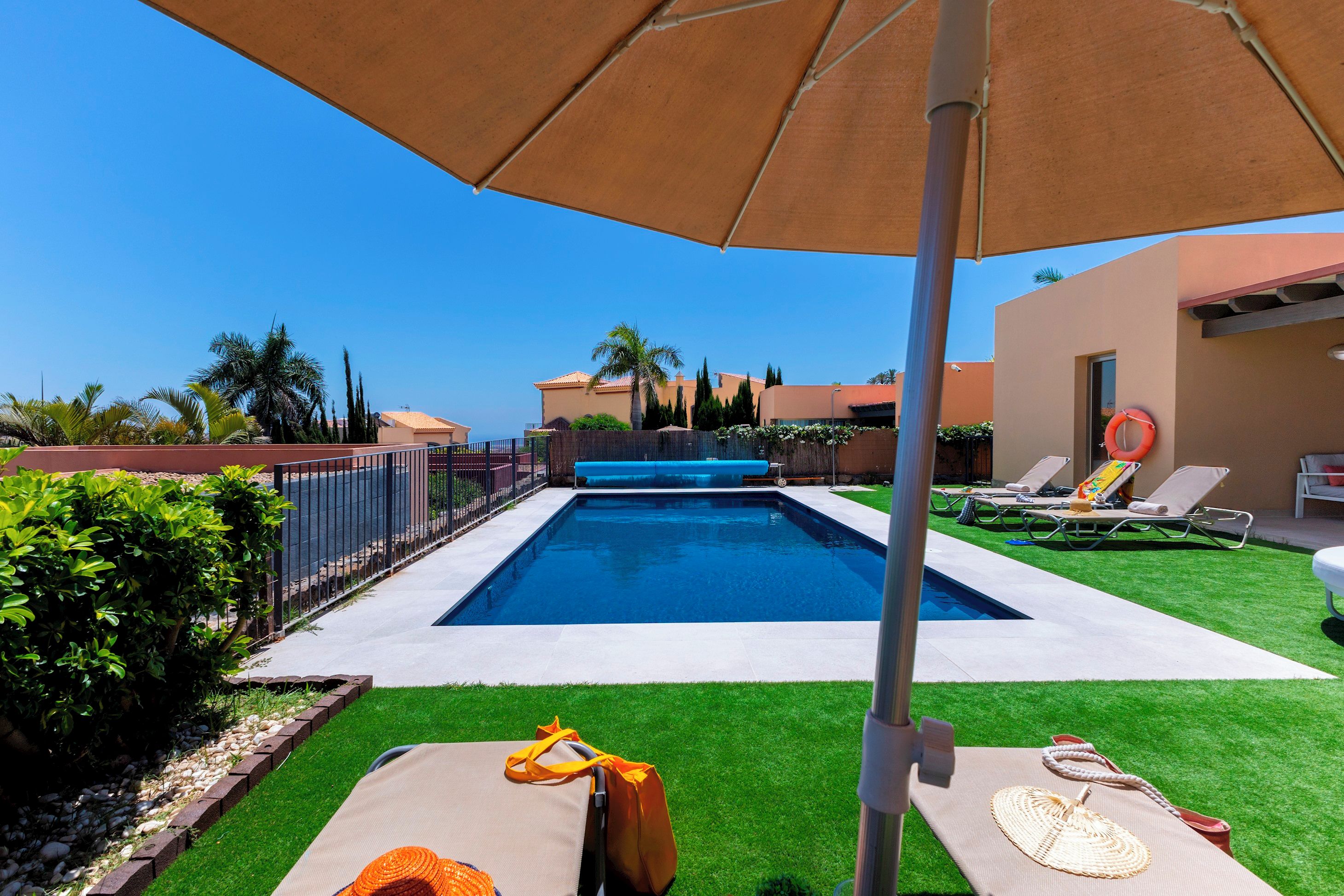 A swimming pool with a clear blue water, surrounded by a well-maintained lawn and a fence.