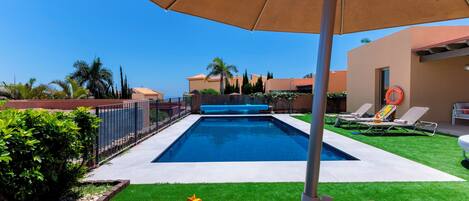 A swimming pool with a clear blue water, surrounded by a well-maintained lawn and a fence.