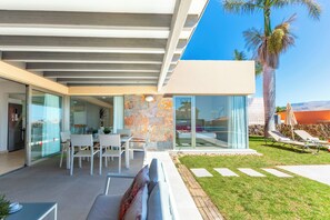 Ein modernes Haus mit Terrasse, Glasüren, einem Essbereich und einem Pool.