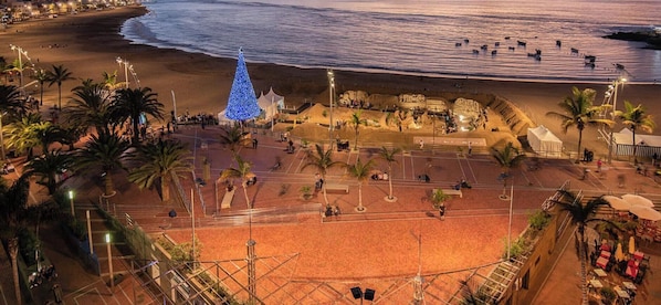 A beachside area with a large blue Christmas tree, palm trees, and a sandy plaza.