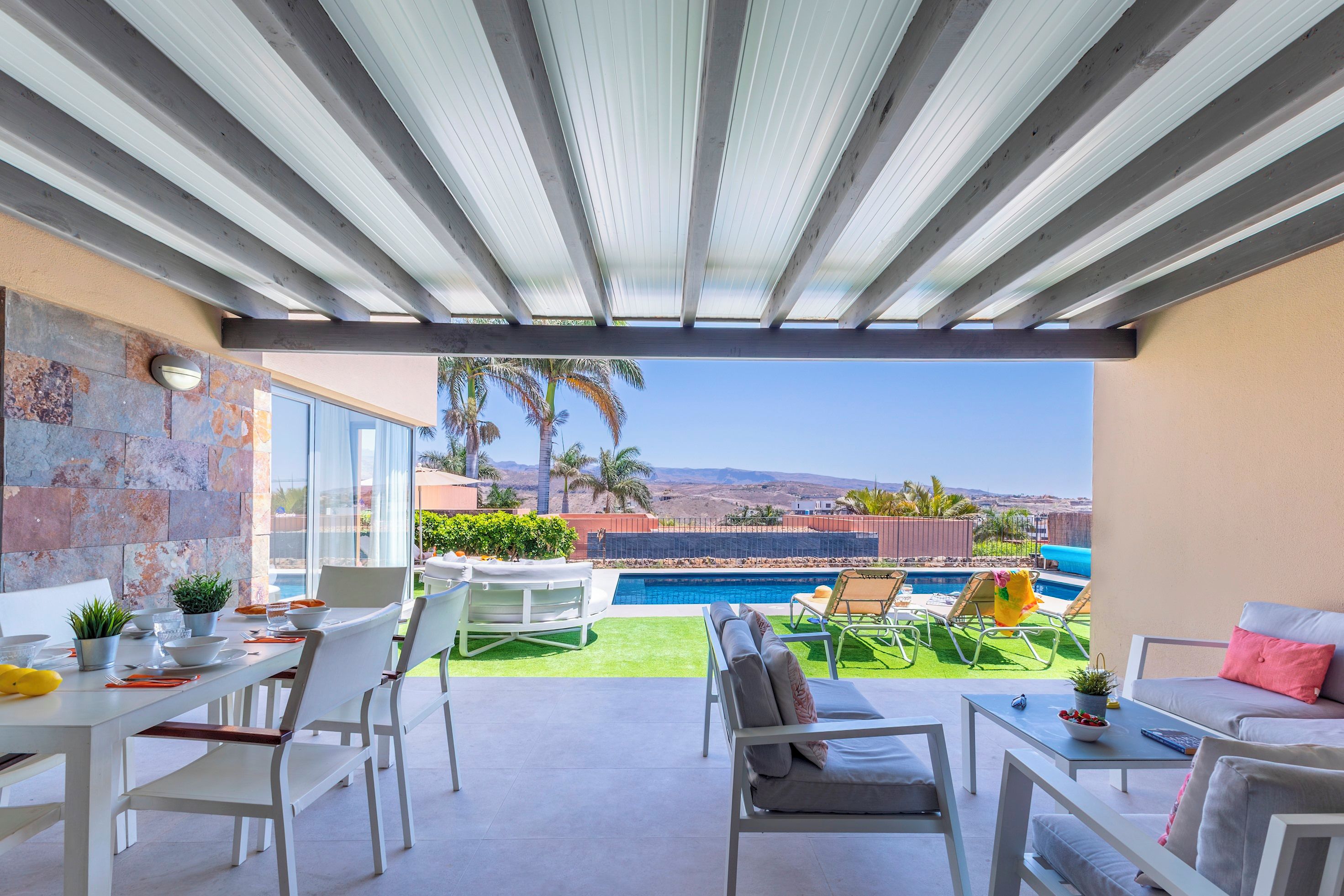Un espacio al aire libre techado con piscina, asientos y vistas al paisaje.
