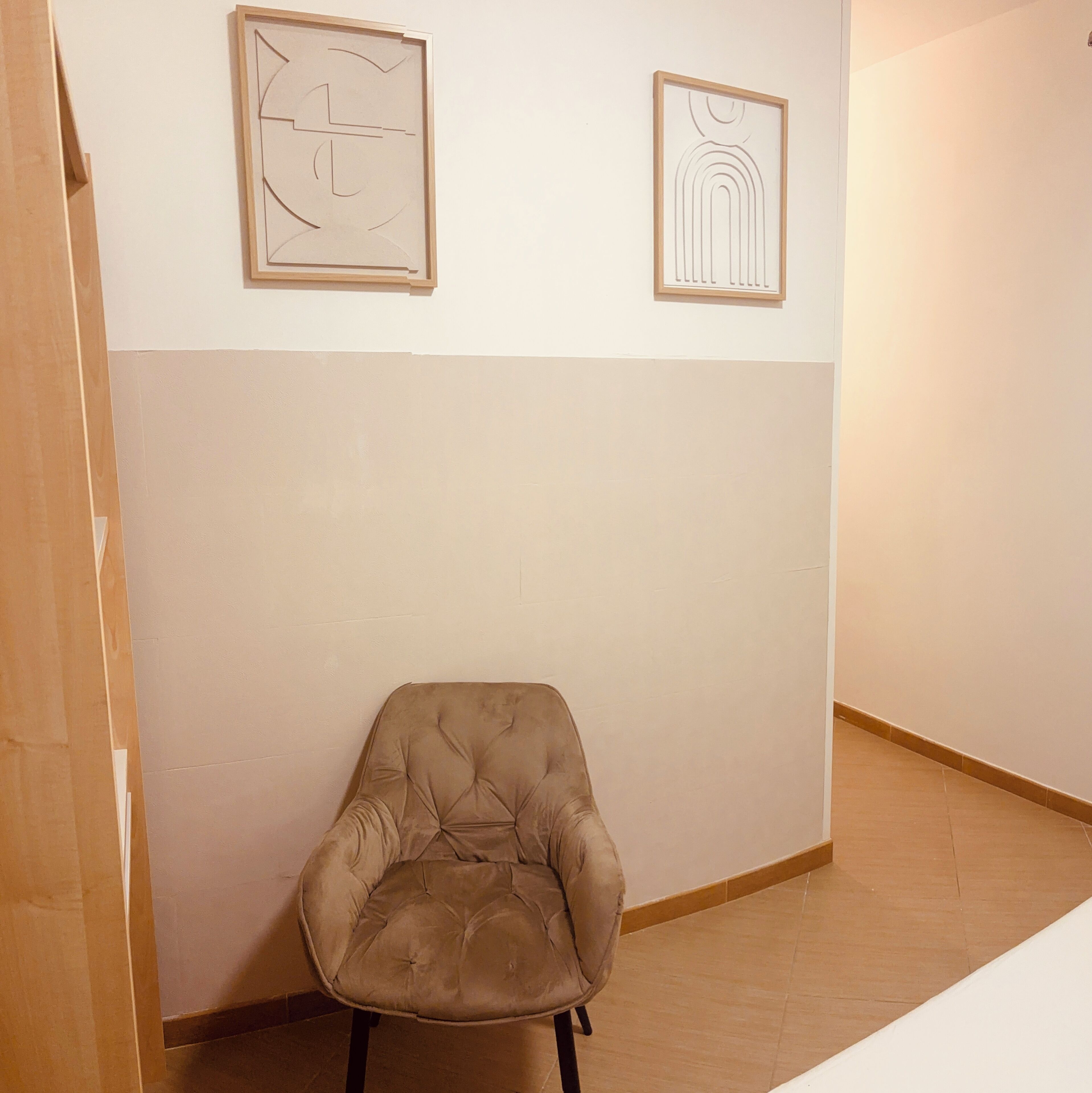 A room with a single chair, two framed artworks on the wall, and a wooden floor.
