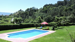 A rectangular swimming pool with a tiled border, surrounded by a grassy area with a few lounge chairs and a red umbrella. - Refuge with swimming pool, playground and incredible views - Pure Tranquillity (celorico de basto)