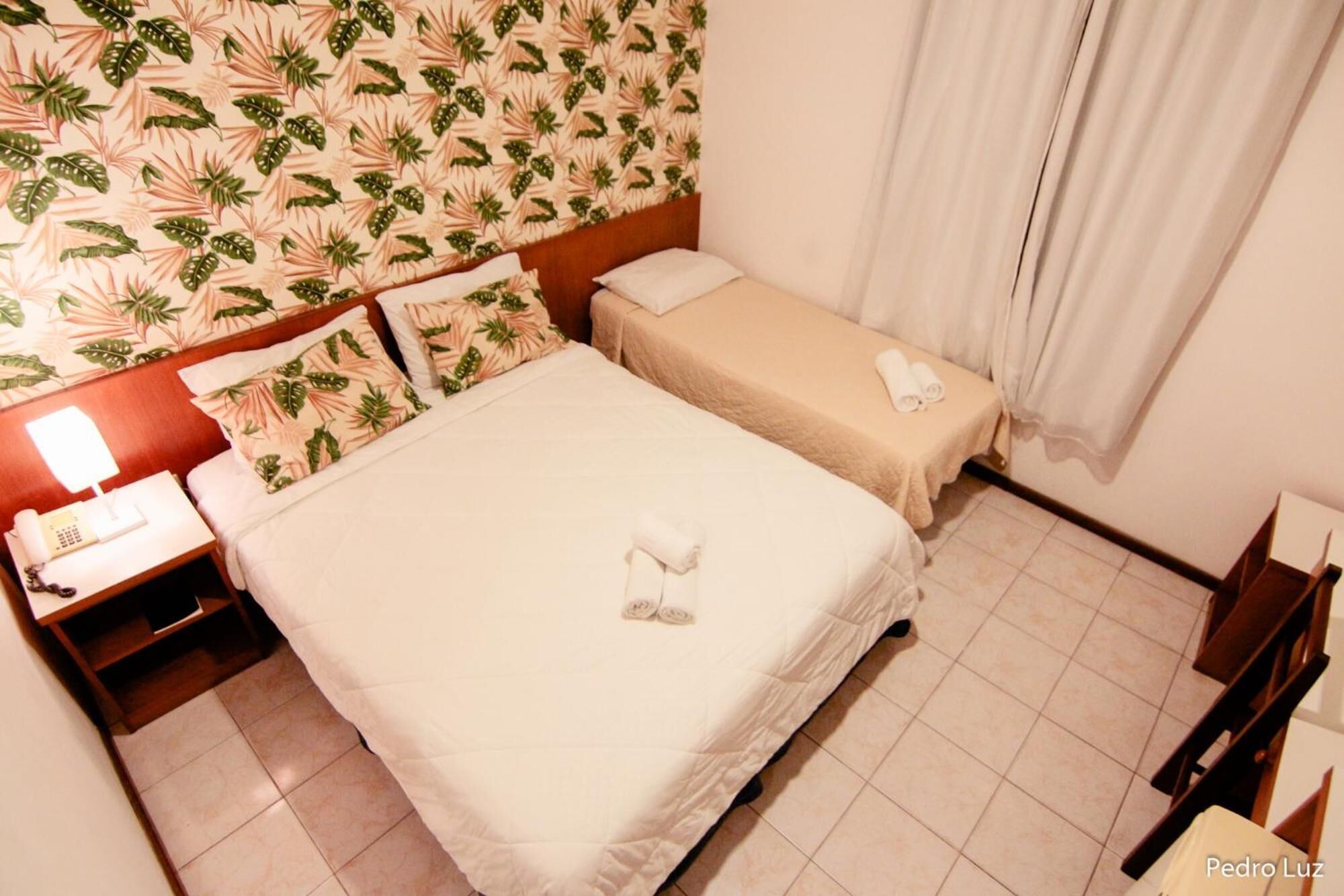 A hotel room with two beds, a nightstand with a lamp, and a telephone.
