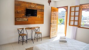 Habitación de hotel con una cama, televisión montada en una pared de madera, dos sillas, una mesita y una ventana con vistas a edificios.