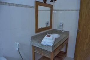 Un baño con lavamanos de encimera de granito, tocador de madera, espejo y toallero.