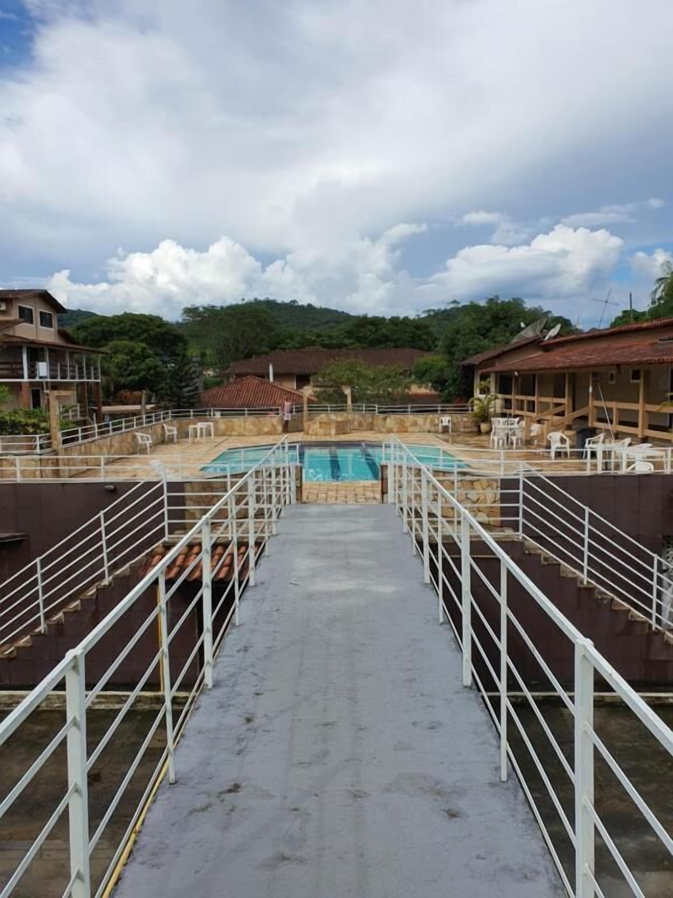 A hotel with a central swimming pool, surrounded by white railings and multiple rooms with red-tiled roofs.