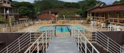 A hotel with a central swimming pool, surrounded by white railings and multiple rooms with red-tiled roofs.