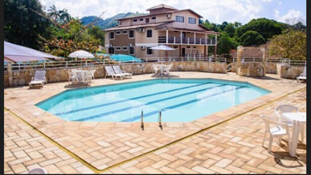 Una piscina con sillones de descanso y sombrillas, rodeada por un muro de piedra y un edificio con varias ventanas.