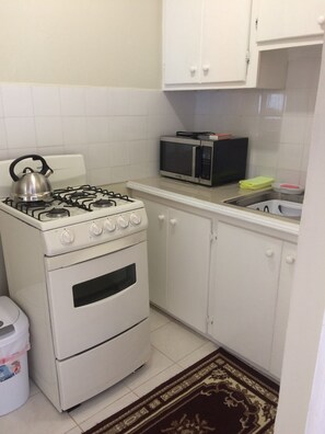 Una cocina con estufa a gas, horno, microondas y armarios blancos.