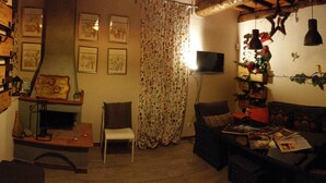 Ein gemütliches Wohnzimmer mit einer Couch, einem Couchtisch und einem Fernseher. An der Wand hängen gerahmte Bilder und ein Vorhang mit floralem Muster.