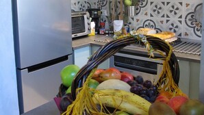 Eine Küche mit einem Edelstahl-Kühlschrank, einer Mikrowelle und einem Herd. Auf der Arbeitsfläche steht eine Obstschale mit verschiedenen Früchten und eine Zierpflanze.