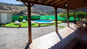 A covered outdoor area with a pool, lounge chairs, and a view of hills. - Charming farmhouse among orange trees (Cónchar)