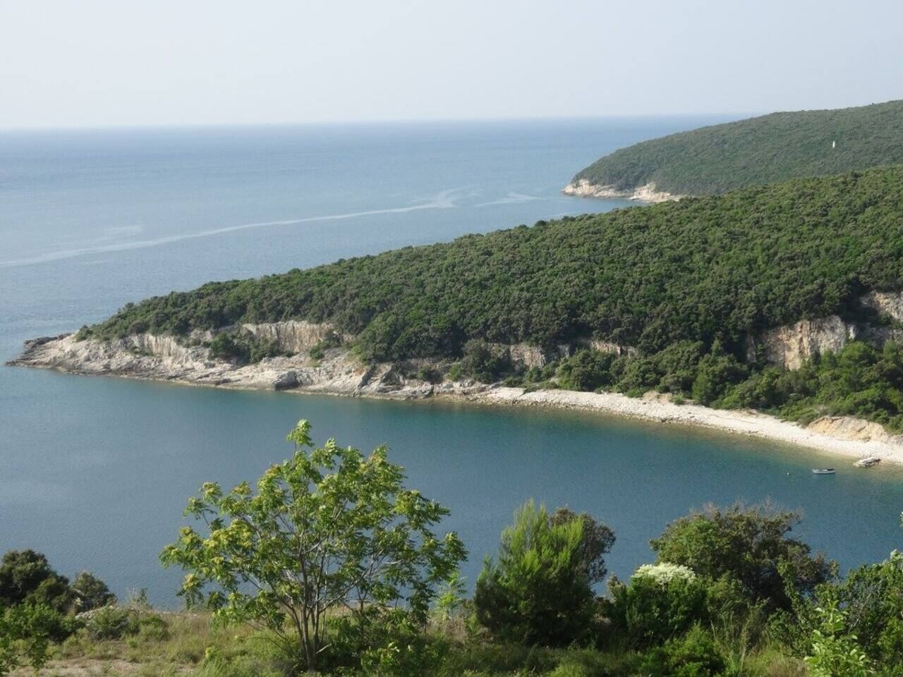 A coastal landscape with a beach, dense greenery, and a clear view of the sea.