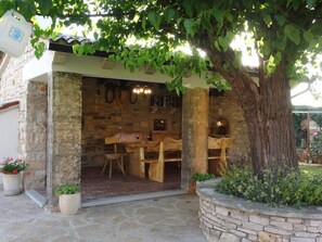 Una estructura de madera al aire libre con un muro de piedra, una mesa, sillas y un colgador de luz.