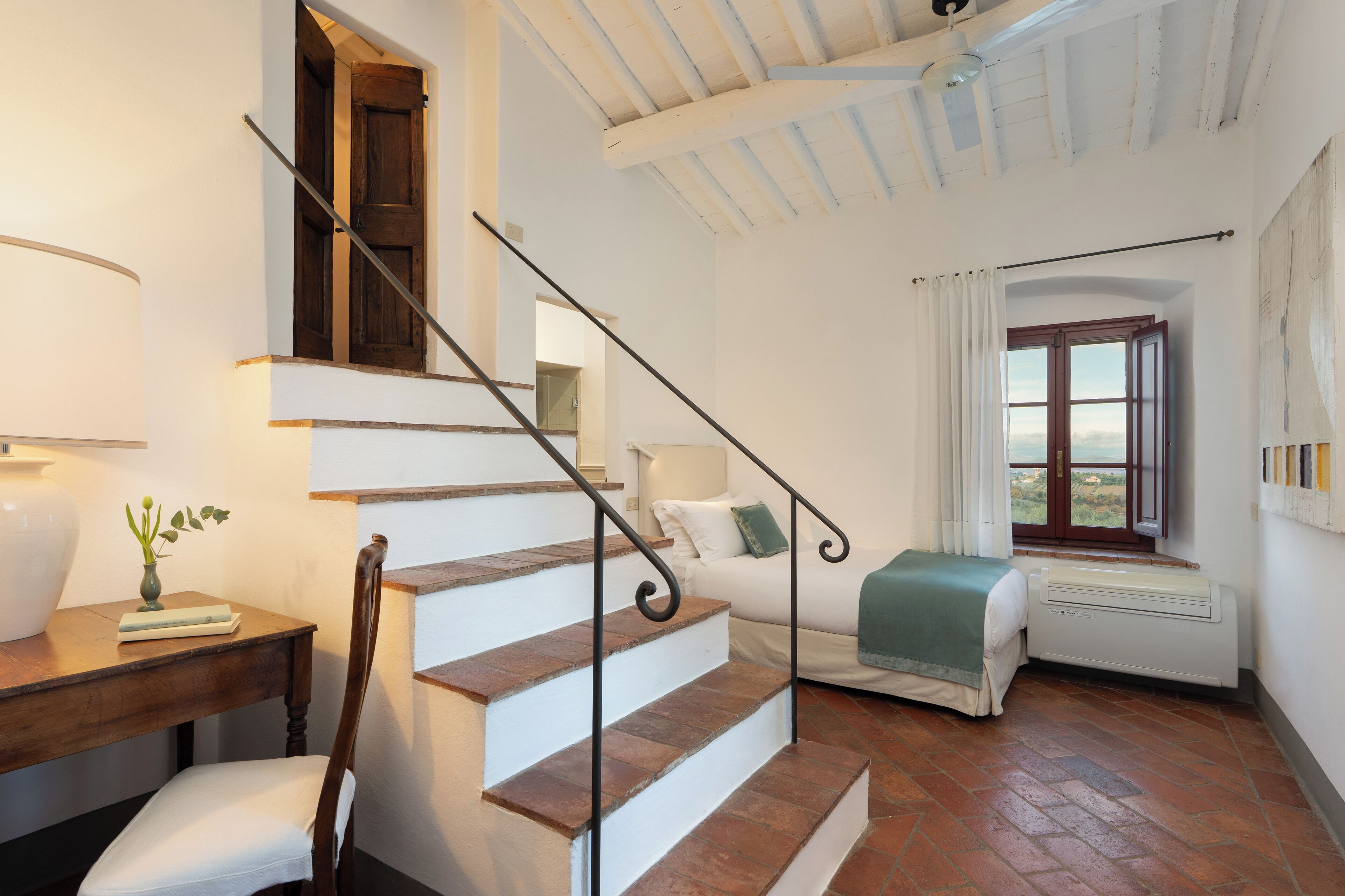 A staircase leading to a bedroom with a bed, a window, and a radiator.