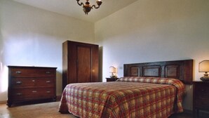 A bedroom with a wooden dresser, a bed with a plaid bedspread, a wooden headboard, and a chandelier.