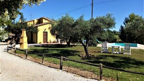 A yellow building with a door and windows, surrounded by a fenced yard with trees and a pool area.