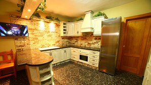 Una cocina con salpicadero de ladrillo, armarios blancos, un refrigerador de acero inoxidable y una puerta de madera.