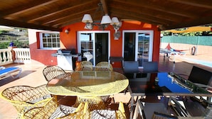 Un patio al aire libre con una mesa redonda y sillas, una parrilla y un área de piscina.