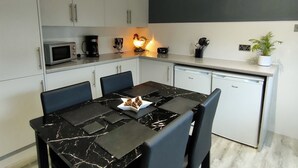 Ett modernt kök med vita skåp, en mikrovågsugn, en kaffebryggare och ett matbord med stolar.